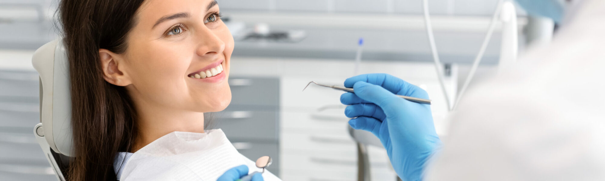 Smiling pretty woman looking at dentist with trust, doctor holding drilling tools, trust and care concept, side view